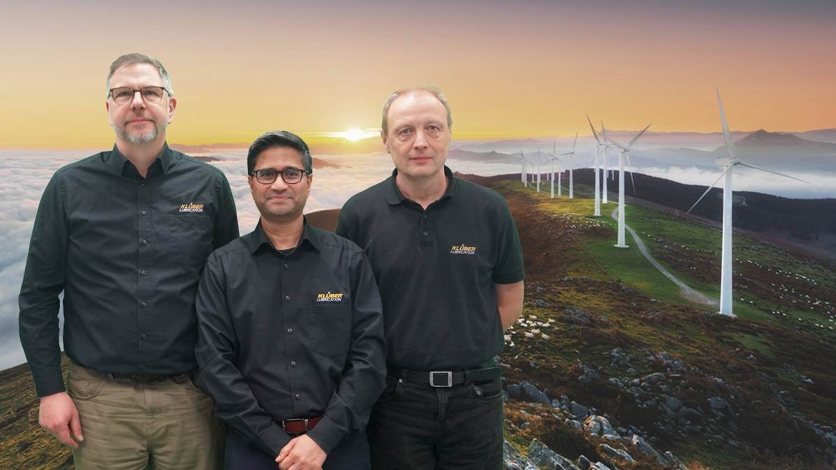 Three men posing in front of wind turbines during sunset