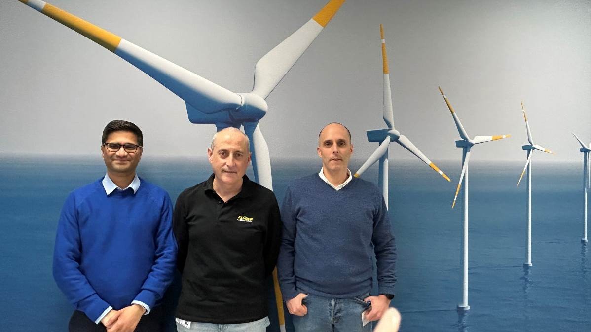 Three men posing in front of wind turbines