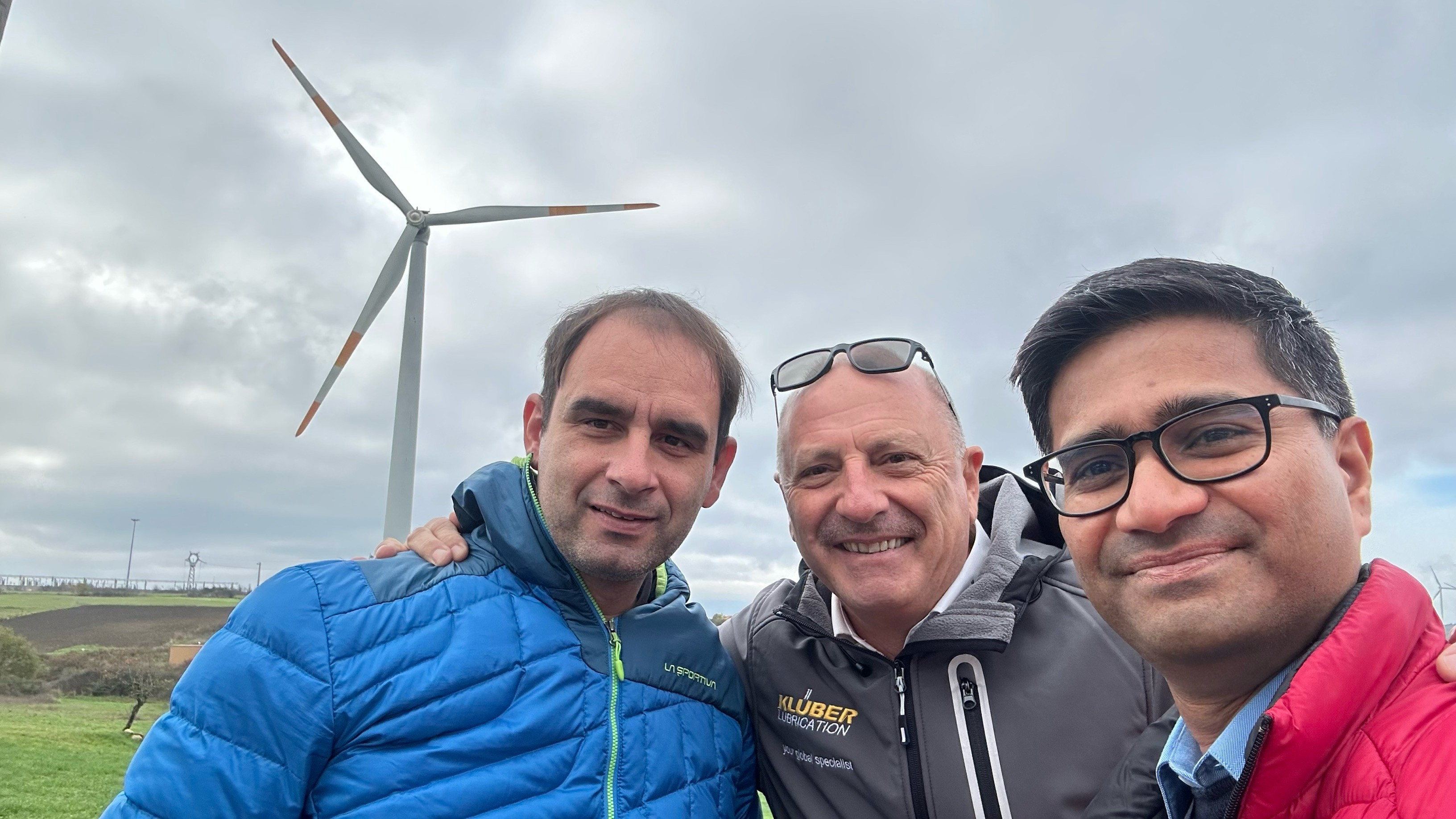 Three men posing in front of a wind turbine