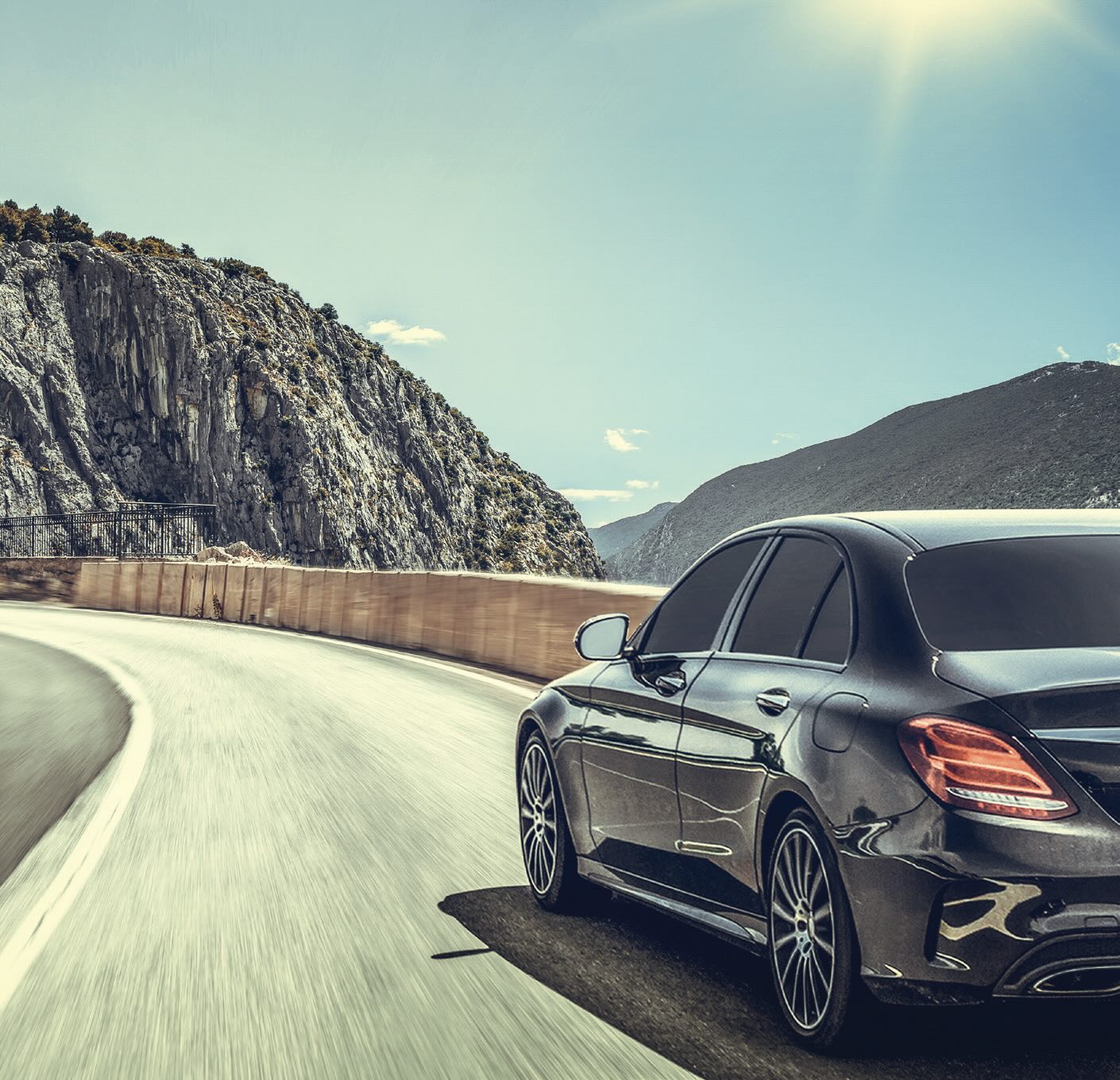 A dark gray car driving on a moutain road on a sunny day.