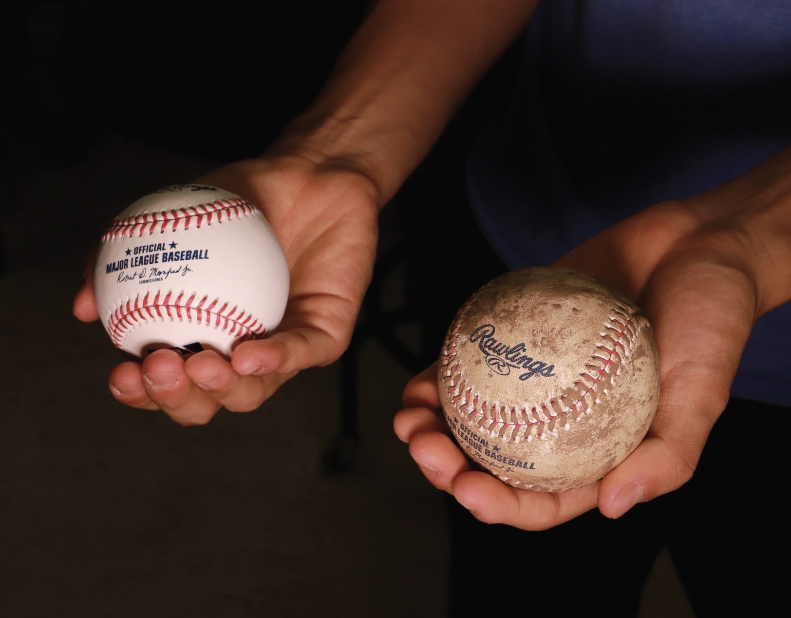 Two hands, one holding a clean baseball and the other holding a dirty baseball