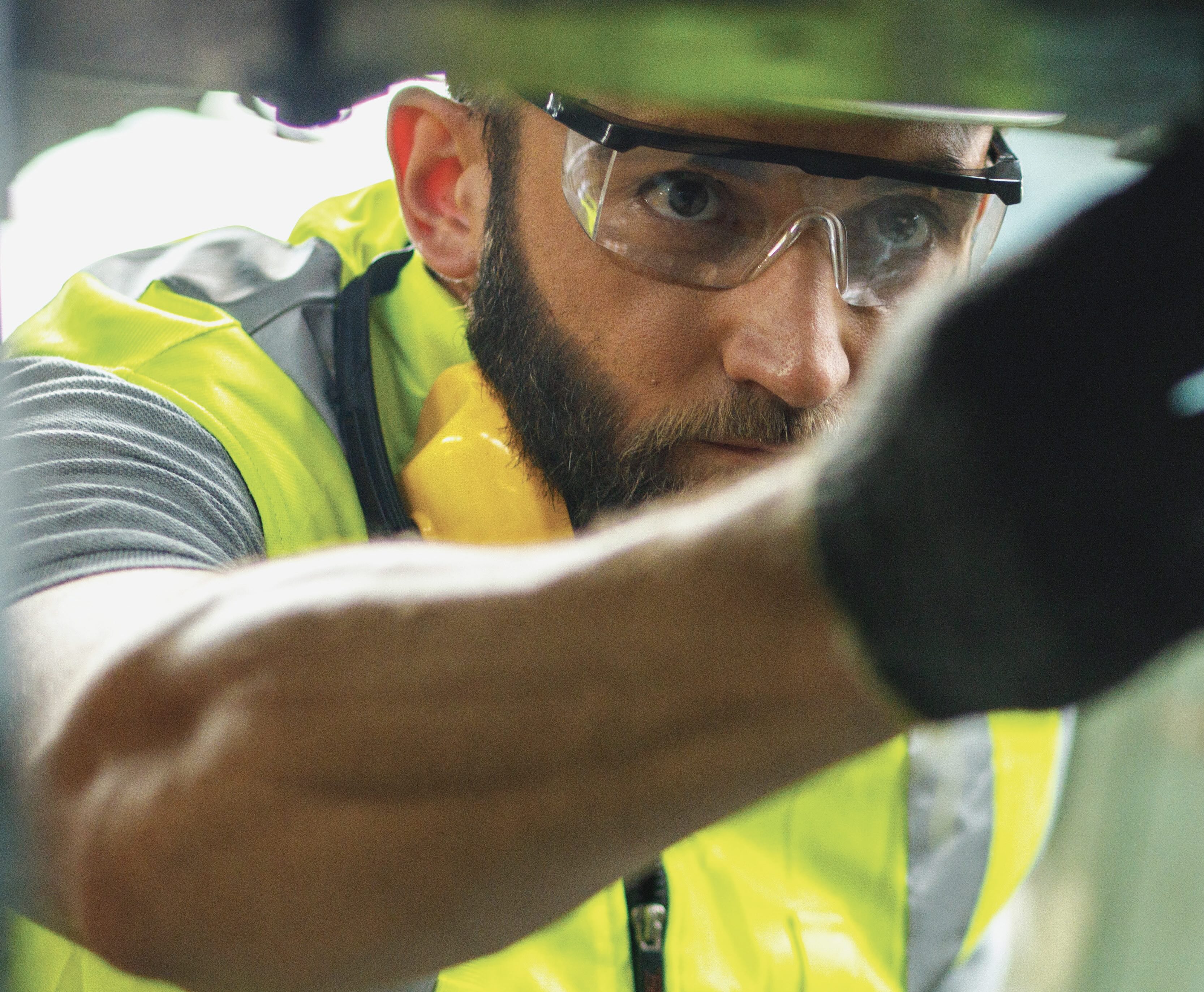 A man wearing a yellow safety vest, gloves and googles