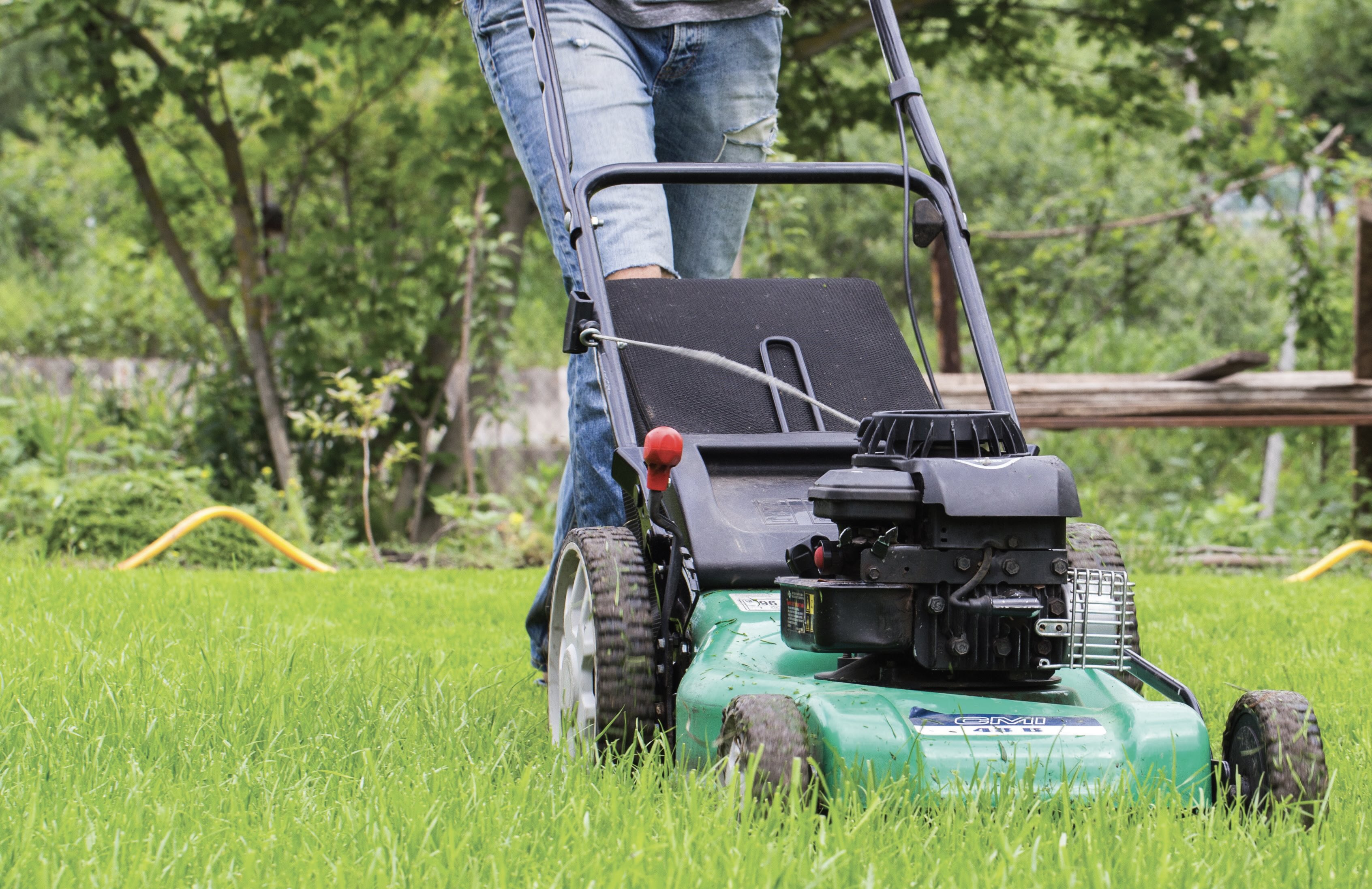 A person in jeans pushes a green lawnmower