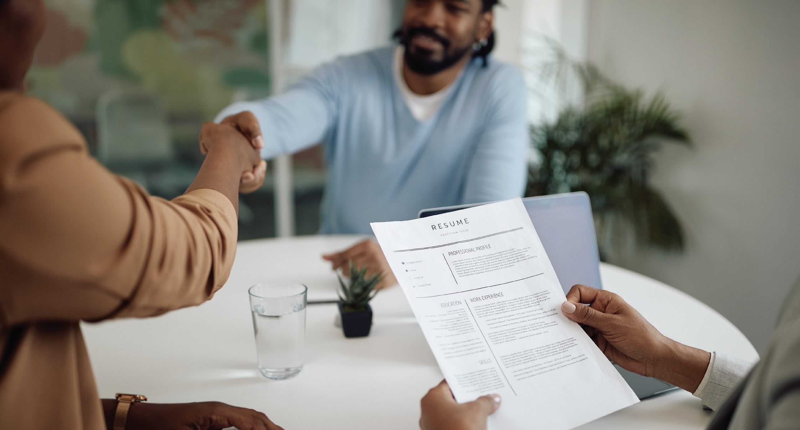 Image of hands holding a paper resume with two people shaking hands in the background