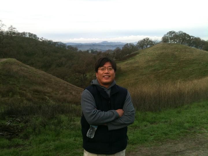 A smiling man with glasses poses in front of a hill.