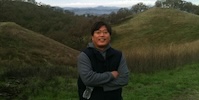 A smiling man with glasses poses in front of a hill.