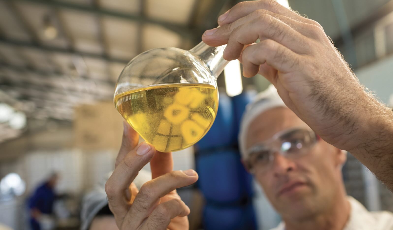 A scientist looks at a beaker full of golden liquid